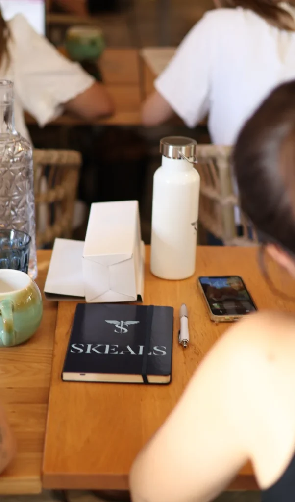 Carnet Skeals posé sur une table de formation, avec stylo, téléphone et gourde, des participantes autour